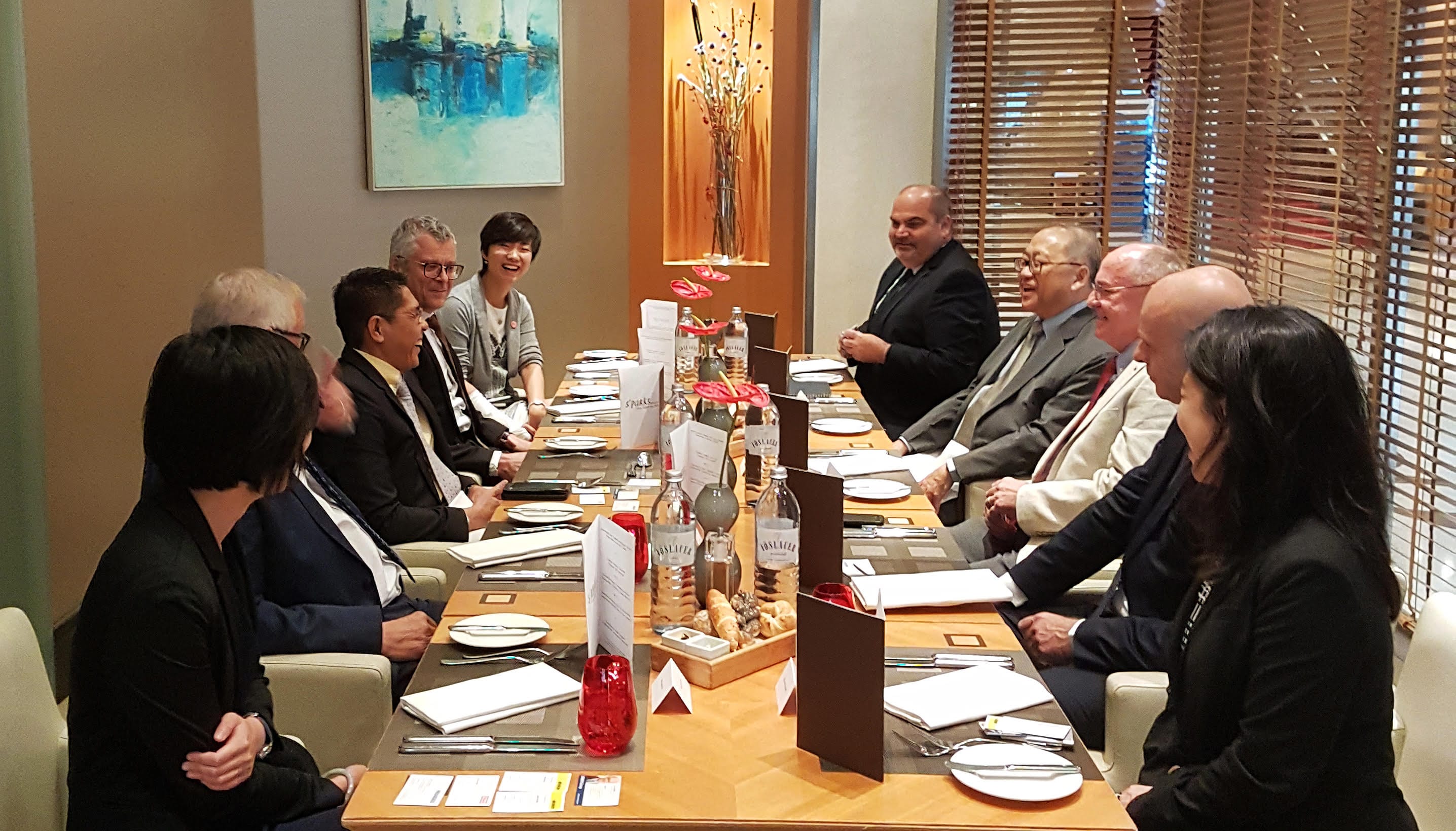 People in business attire sit at a set table with water bottles and menus.
